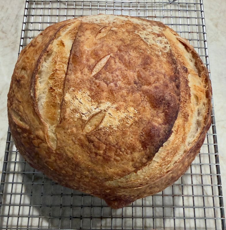 A golden sourdough loaf with scored crust cooling on a wire rack