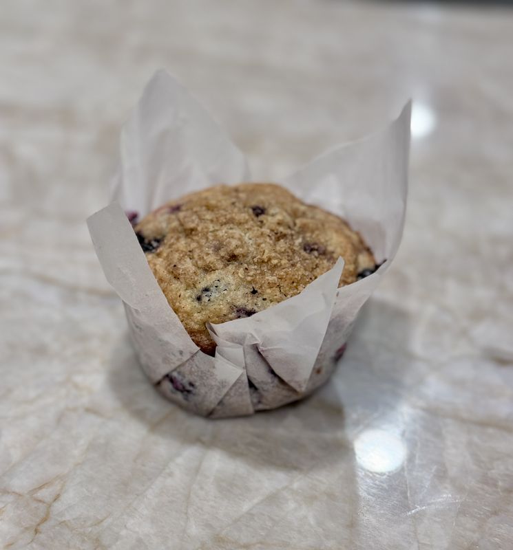 A blueberry streusel muffin in a tulip paper liner